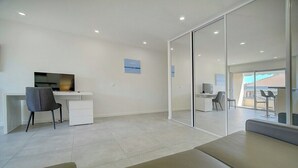 Une pièce moderne et bien éclairée, équipée d’un bureau, d’une chaise et d’une grande porte-fenêtre coulissante donnant sur un espace extérieur.