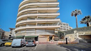 Un immeuble à plusieurs étages doté de balcons, d’un espace de stationnement et de palmiers.