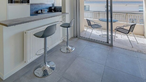 Une cuisine moderne avec un coin bar, deux tabourets de bar et une vue sur un balcon aménagé avec des sièges d’extérieur.