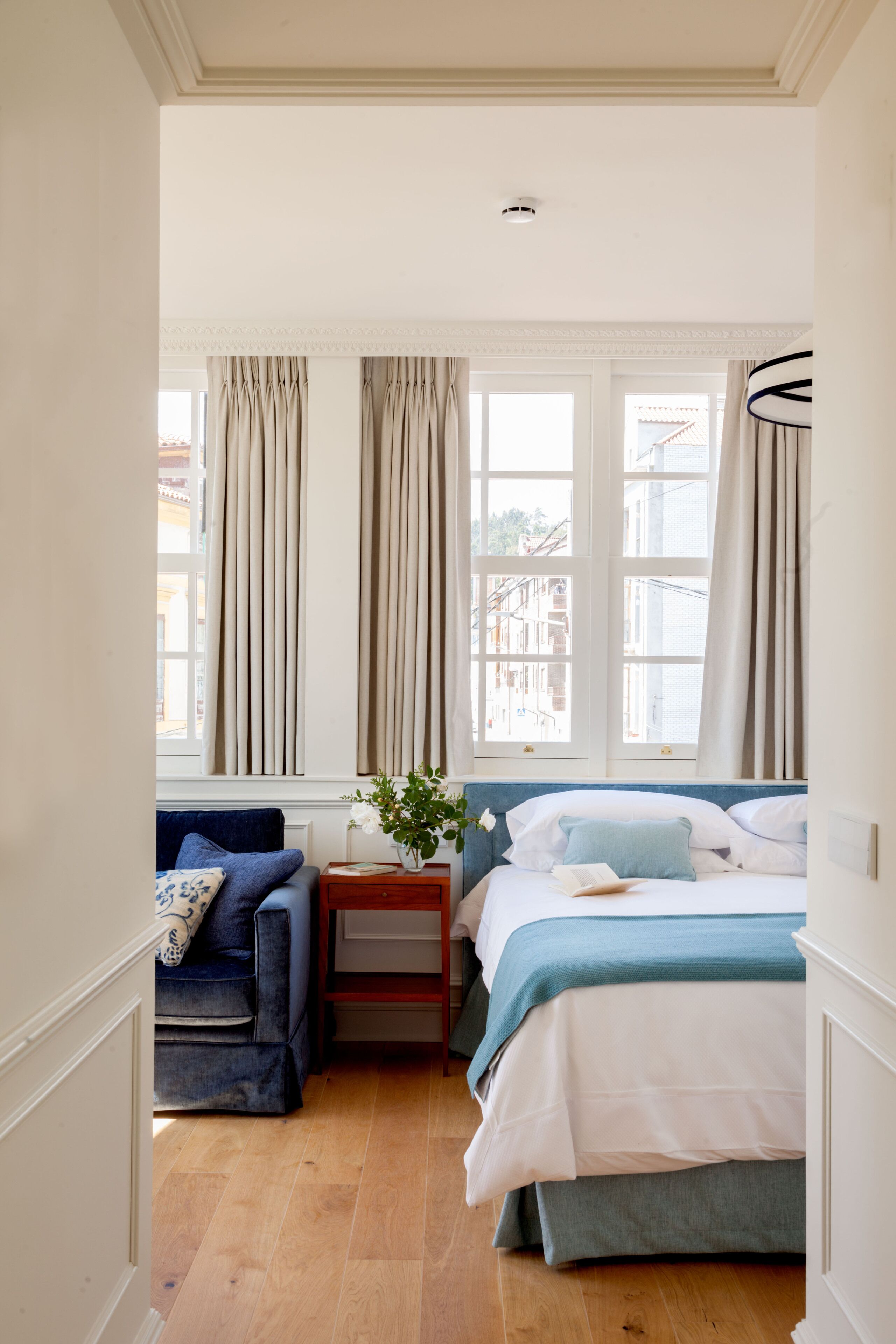 A bedroom with a bed, a sofa, a nightstand, and a window with curtains.