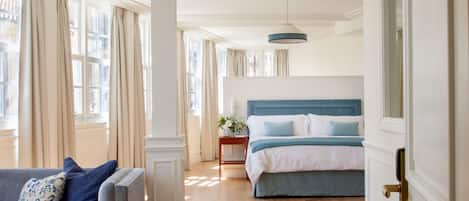 Un dormitorio amplio con una cama grande, una zona de estar con sofá y vistas a la ciudad a través de amplias ventanas.