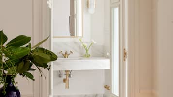 Pasillo que conduce a un baño con lavamanos de mármol, un espejo y un cubo de basura.