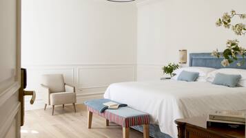 A bedroom with a bed, a bench, a chair, a bedside table, and a hanging light fixture.