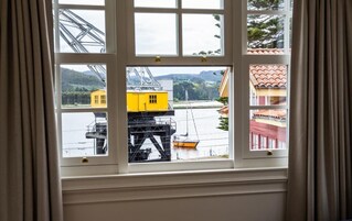 A window with a view of a yellow crane and a sailboat on a body of water, with buildings in the background.