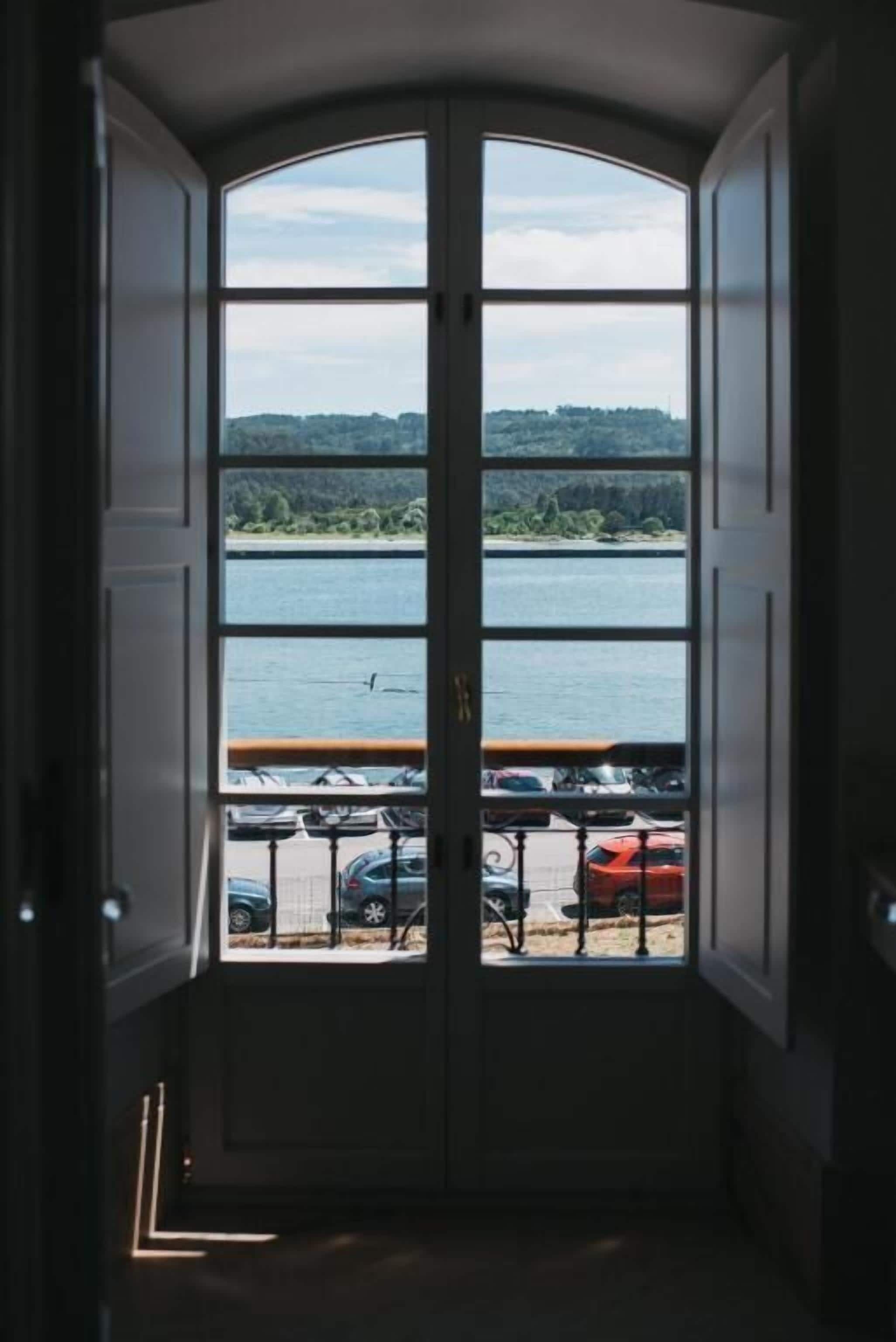 A view through a bay window with a lake and parked cars visible.