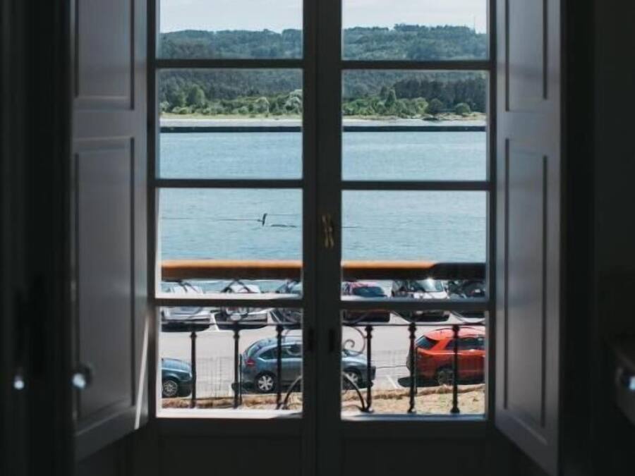 Vista a través de un ventanal con un lago y coches aparcados.