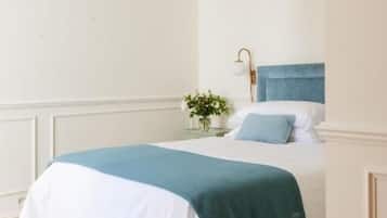 Una cama bien tendida con edredón azul y blanco, una mesita de noche con lámpara, y un colgante de techo.