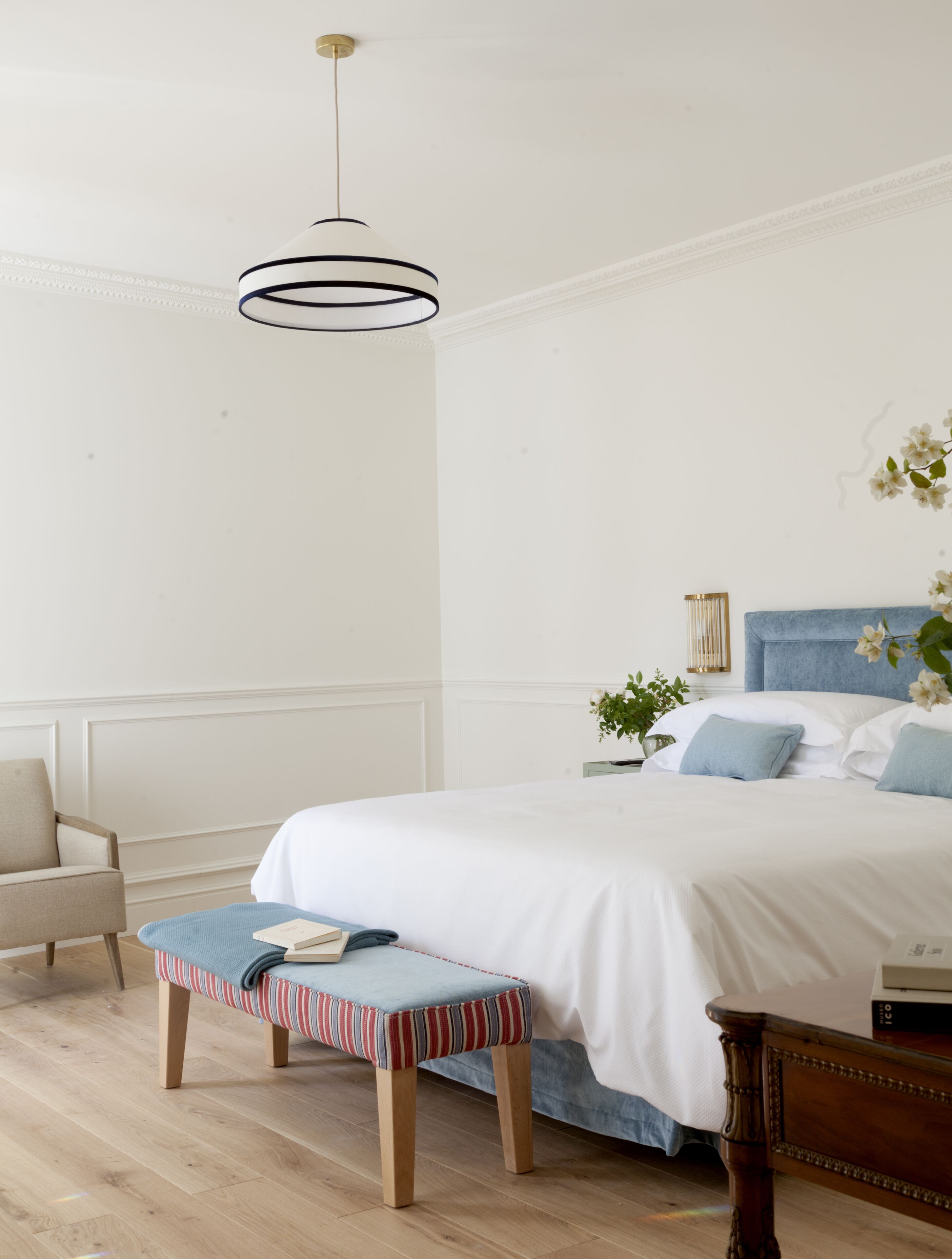 A bedroom with a large bed, a bedside table with a lamp, a chair, and a striped bench.