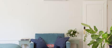 A room with a blue sofa, a small side table, a glass table with a vase, and a white door.
