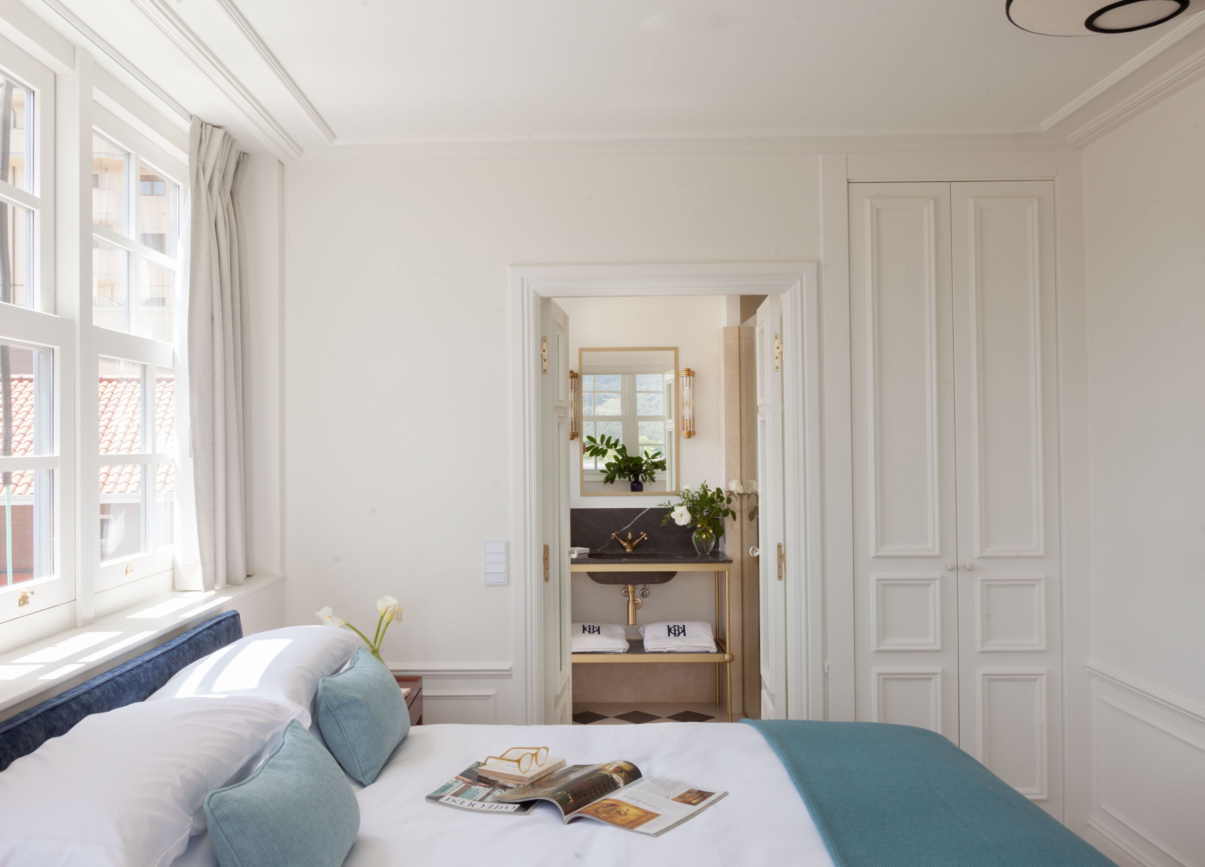 A hotel room with a bed, a vanity with a mirror, and a view of the outside through a window.