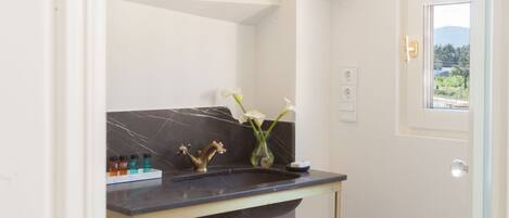 A bathroom with a marble sink, a towel rack with towels, and a view of greenery outside.
