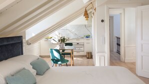 A bedroom with a large bed, a desk, and a view of a kitchen and balcony. - Gran Hotel Brillante (Muros de Nalon)