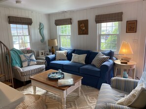 A cozy living room with a blue sofa, striped armchairs, a wooden coffee table, and a lamp on a side table. - Walk to the Beach! (Dennis Port)