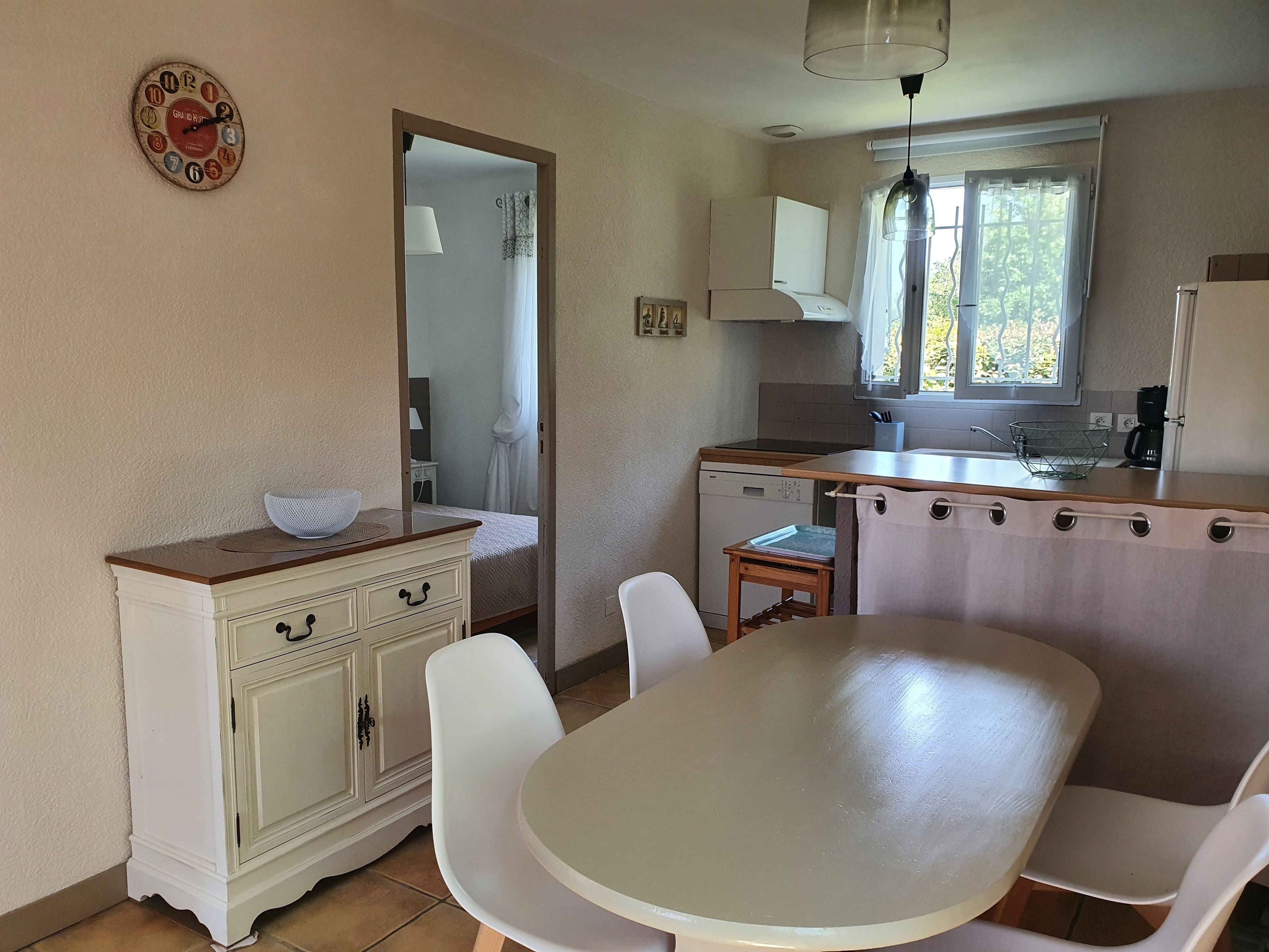 A compact kitchen with a dining area, a white cabinet, a sink, and a window with curtains.