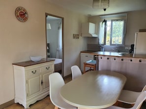 Eine kleine Küche mit Essbereich, einem weißen Schrank, einer Spüle und einem Fenster mit Vorhängen.