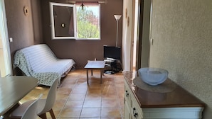Una habitación compacta con cama, una mesita, televisor y kitchenette.