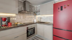 A modern kitchen with a red refrigerator, built-in oven, and a stainless steel range hood. - Fantastic Penthouse in Neos Marmaras (Sithonia)