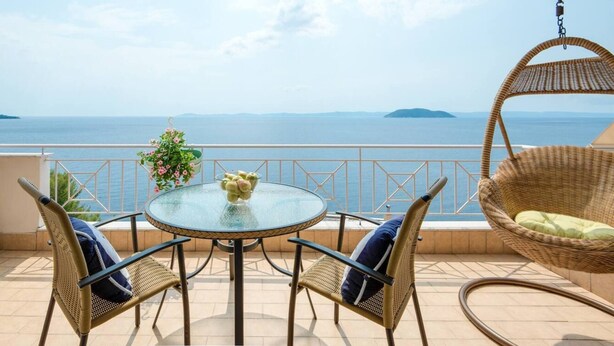 A balcony with a glass table, wicker chairs, and a hanging chair overlooking a sea view. - Fantastic Penthouse in Neos Marmaras (Sithonia)