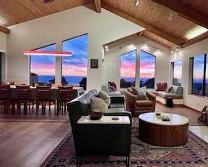 Ein großzügiger Wohnbereich mit Esstisch, Sofas und Couchtisch. Große Fenster bieten Blick auf den Ozean.