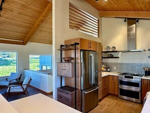 A modern kitchen with built-in appliances, wooden cabinetry, and a view of the outdoors. - Cormorant Cove | Ocean Views, Hot Tub & EV Charger (Sea Ranch)