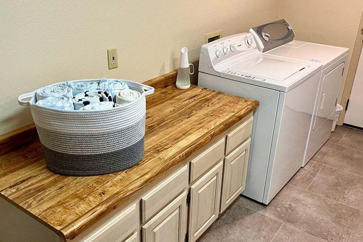Een wasruimte met een wasmachine, een droogmachine en een mandje gevouwen kleding op een houten aanrecht.