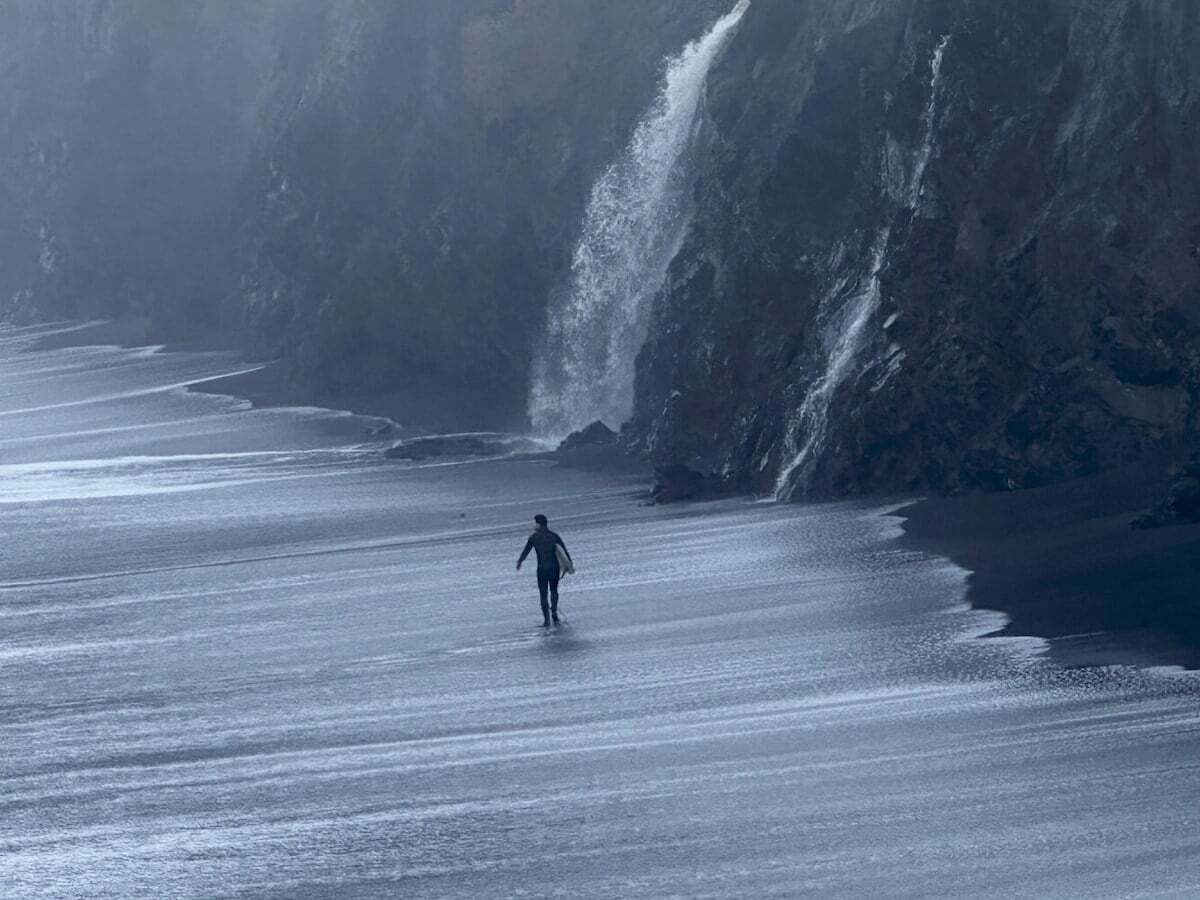 A person walking on a beach with a large wave in the background.