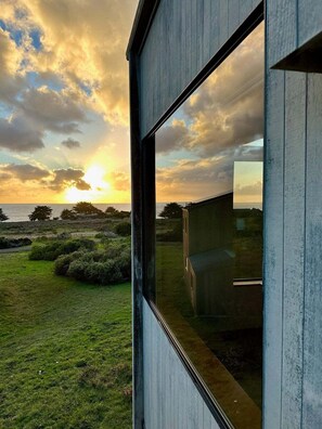 A modern building with a large window reflecting a sunset over a grassy landscape.