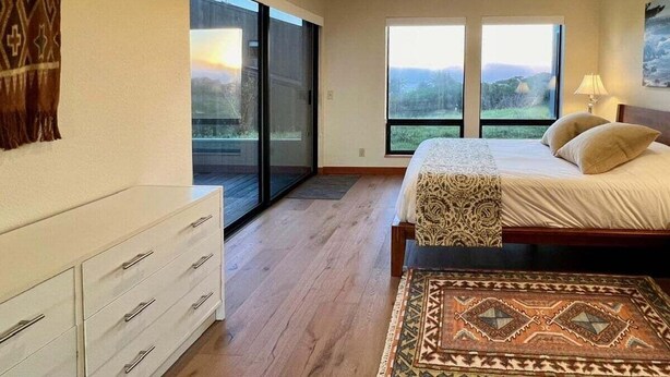 A bedroom with a large bed, a nightstand, a dresser, and a view of the outdoors through a sliding glass door.