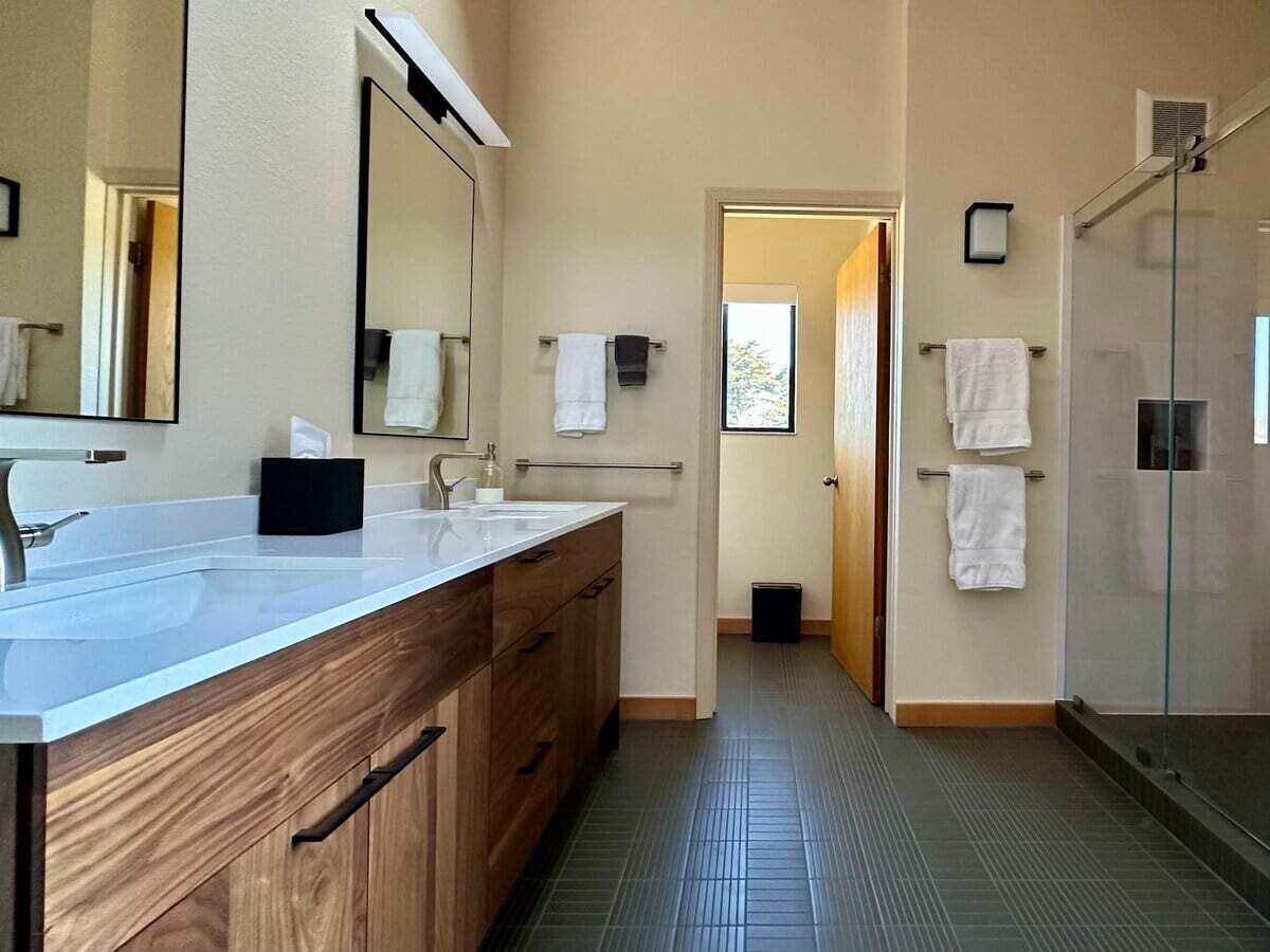 Ein modernes Badezimmer mit einem Doppelwaschtisch, einer Duschkabine aus Glas und einer sichtbaren Tür zu einem anderen Raum.