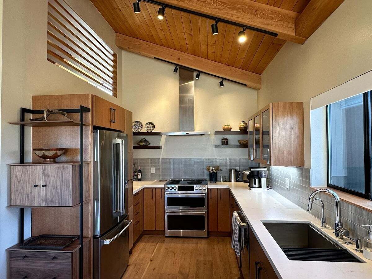 A modern kitchen with wooden cabinets, stainless steel appliances, and a large window.