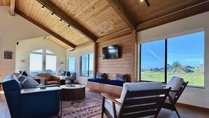 A spacious living room with a high ceiling, large windows, and a view of the outdoors.
