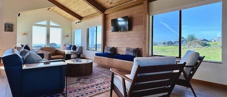 Een ruime woonkamer met een hoge plafond, grote ramen en uitzicht op het landschap.