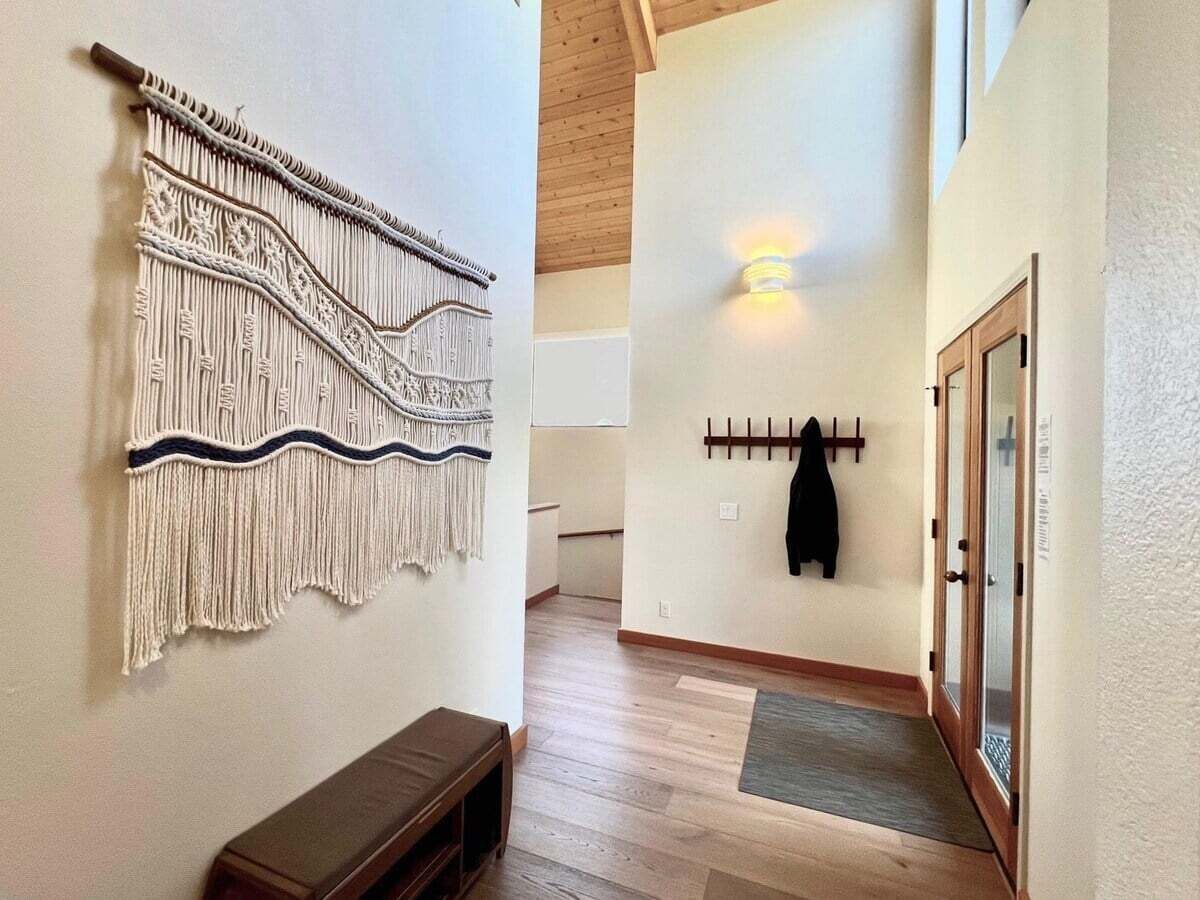 A hallway with a macrame wall hanging, a coat rack with a jacket, and a bench.