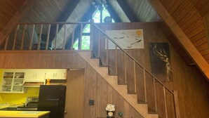 Un intérieur en bois avec un escalier menant à une mezzanine, une cuisine équipée d’armoires et un lustre.