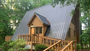 Une cabane dotée d’un toit à forte pente, d’une terrasse en bois et d’un petit porche.