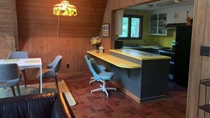 Une cuisine chaleureuse avec un plafond en bois, un coin repas avec une table et des chaises, et un petit îlot central doté d’un évier.