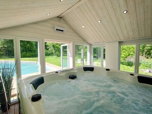 A hot tub with a view of a swimming pool and greenery outside. - Contemporary villa with a pool, spa, and sauna in the heart of unspoiled nature (Rumilly)