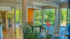 Amplia habitación con ventanas grandes, una mesa de vidrio y vistas al verde exterior.