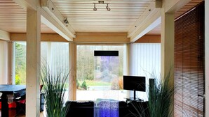 Una habitación moderna con un ventanal grande, un televisor negro y dos plantas altas.