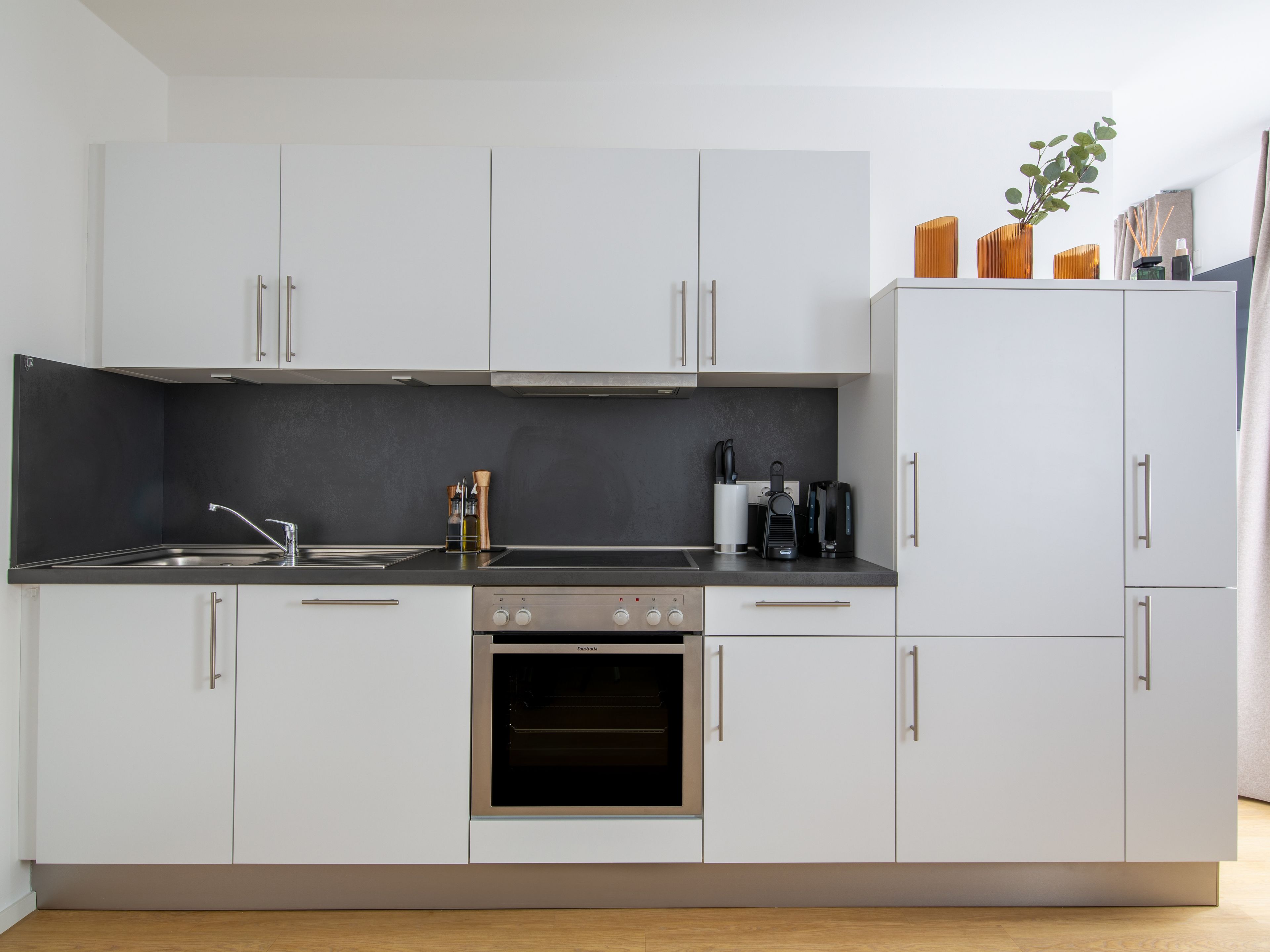 Een moderne keuken met witte kastjes, een zwart aanrecht en roestvrijstalen apparatuur, waaronder een oven en een koffiezetapparaat.