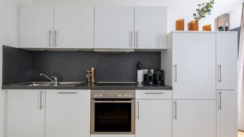 Een moderne keuken met witte kastjes, een zwart aanrecht en roestvrijstalen apparatuur, waaronder een oven en een koffiezetapparaat.