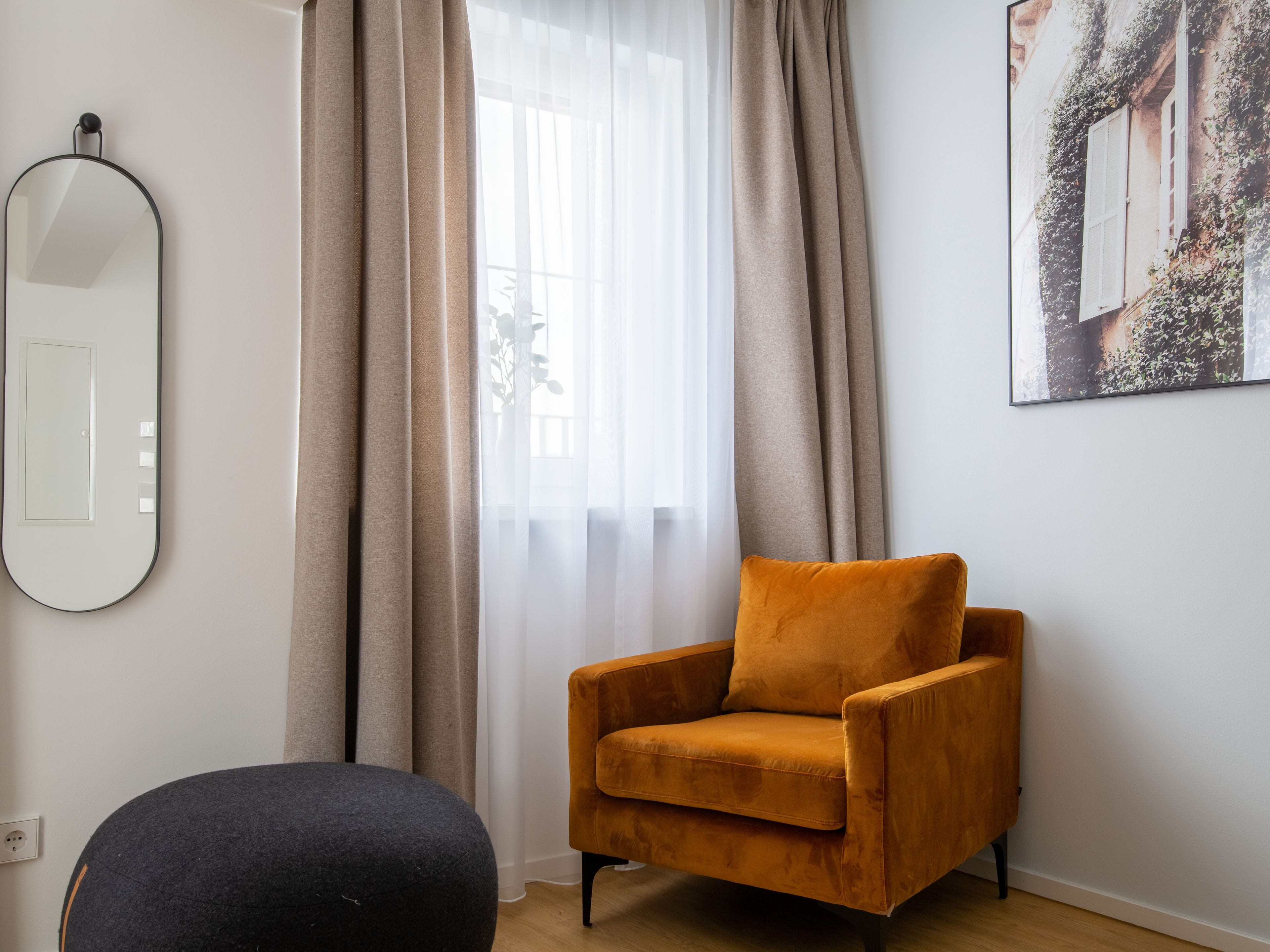Ein Zimmer mit einer Couch, einem Sessel, einem Spiegel und einem Fenster mit Vorhängen.