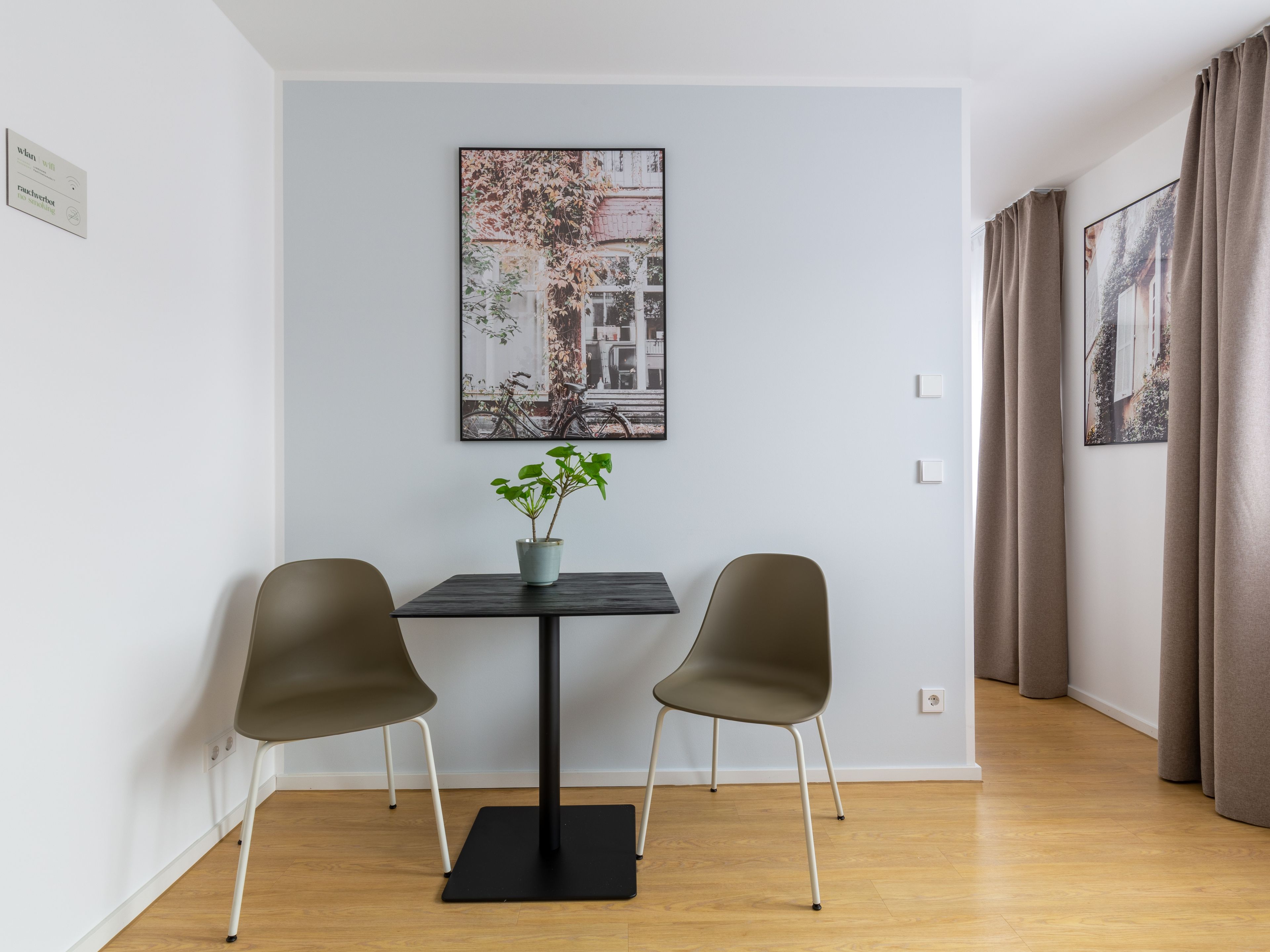 A room with a table, two chairs, a potted plant, and two framed pictures on the wall.