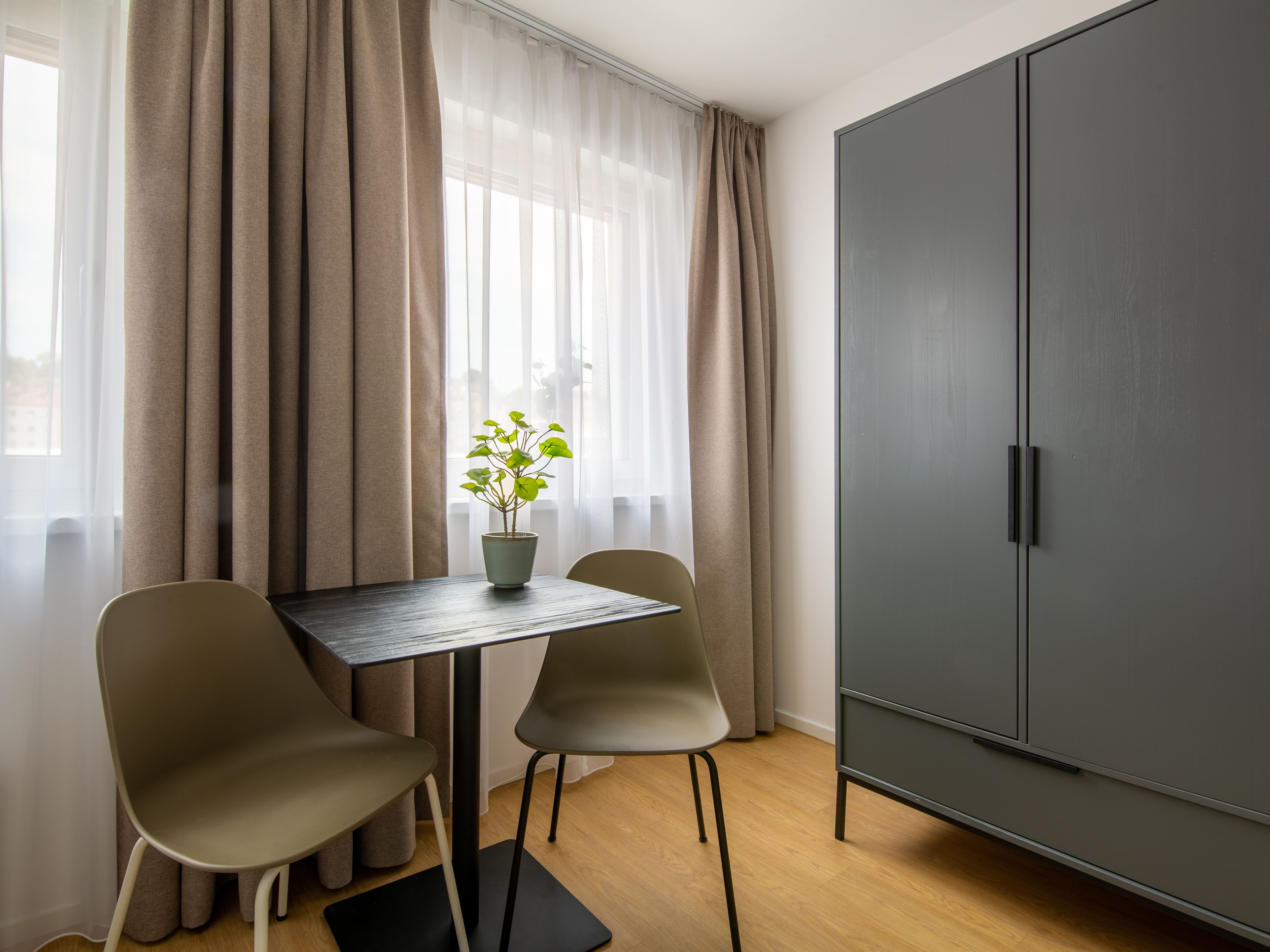 Ein Zimmer mit Esstisch, zwei Stühlen, einer Zimmerpflanze und einem Kleiderschrank.