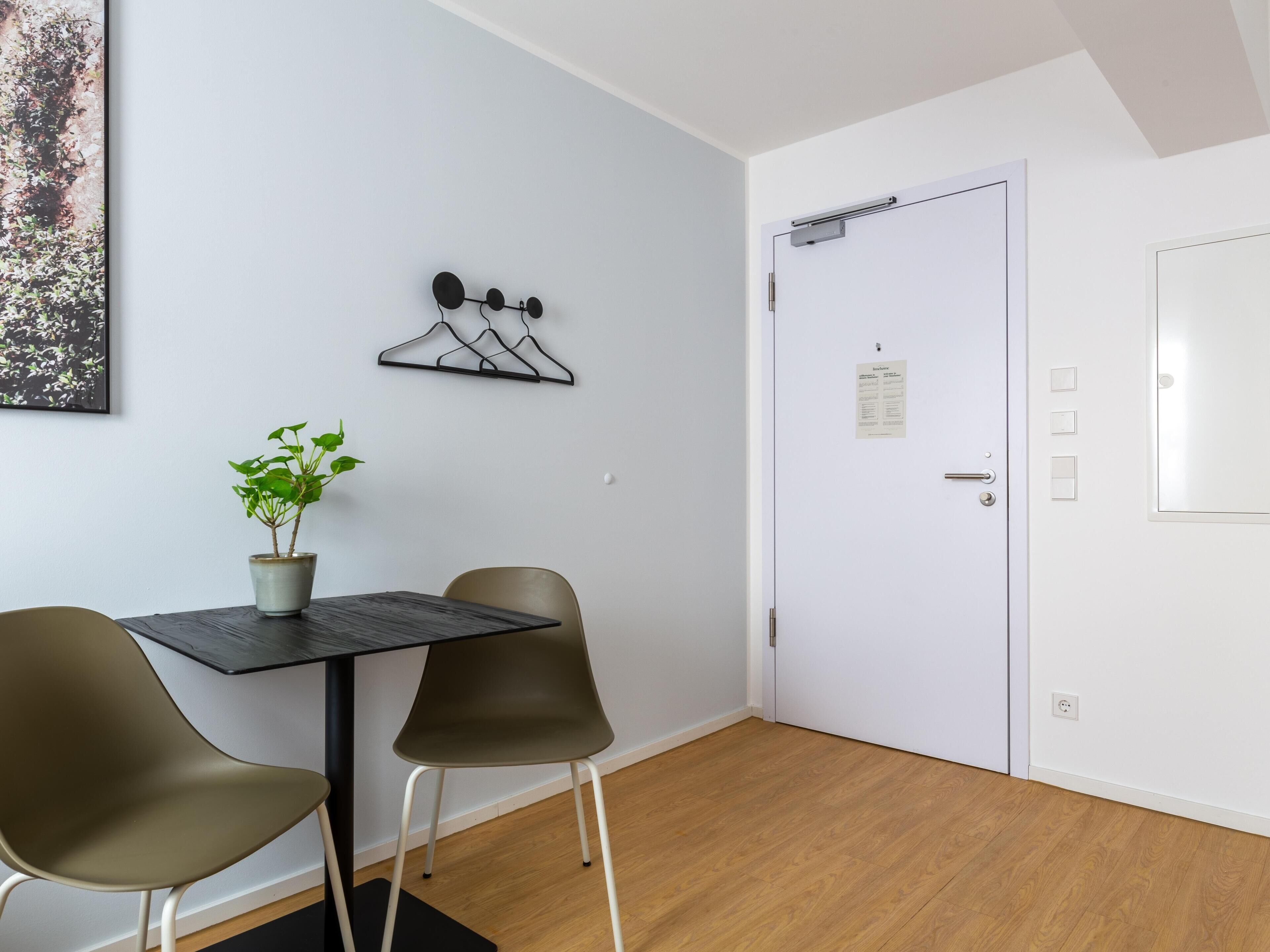 A room with a table, two chairs, a potted plant, a coat rack, and a white door with a notice on it.