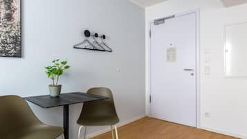 A room with a table, two chairs, a potted plant, a coat rack, and a white door with a notice on it.