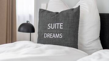 A hotel room with a bed, a pillow with "SUITE DREAMS" embroidered, a lamp, and a wall with a framed picture.