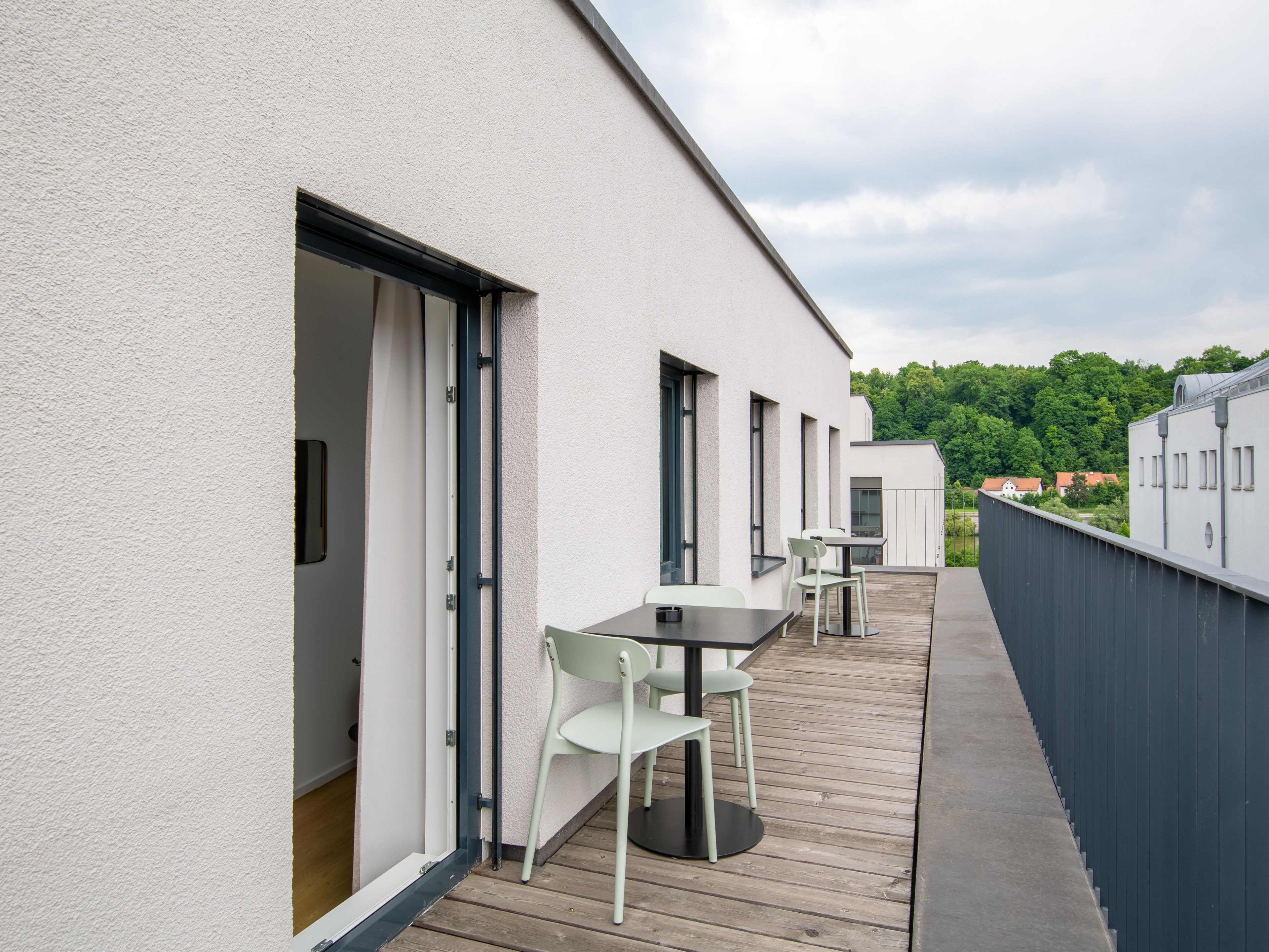 A modern outdoor deck with a table and chairs, a wooden floor, and a white building facade.
