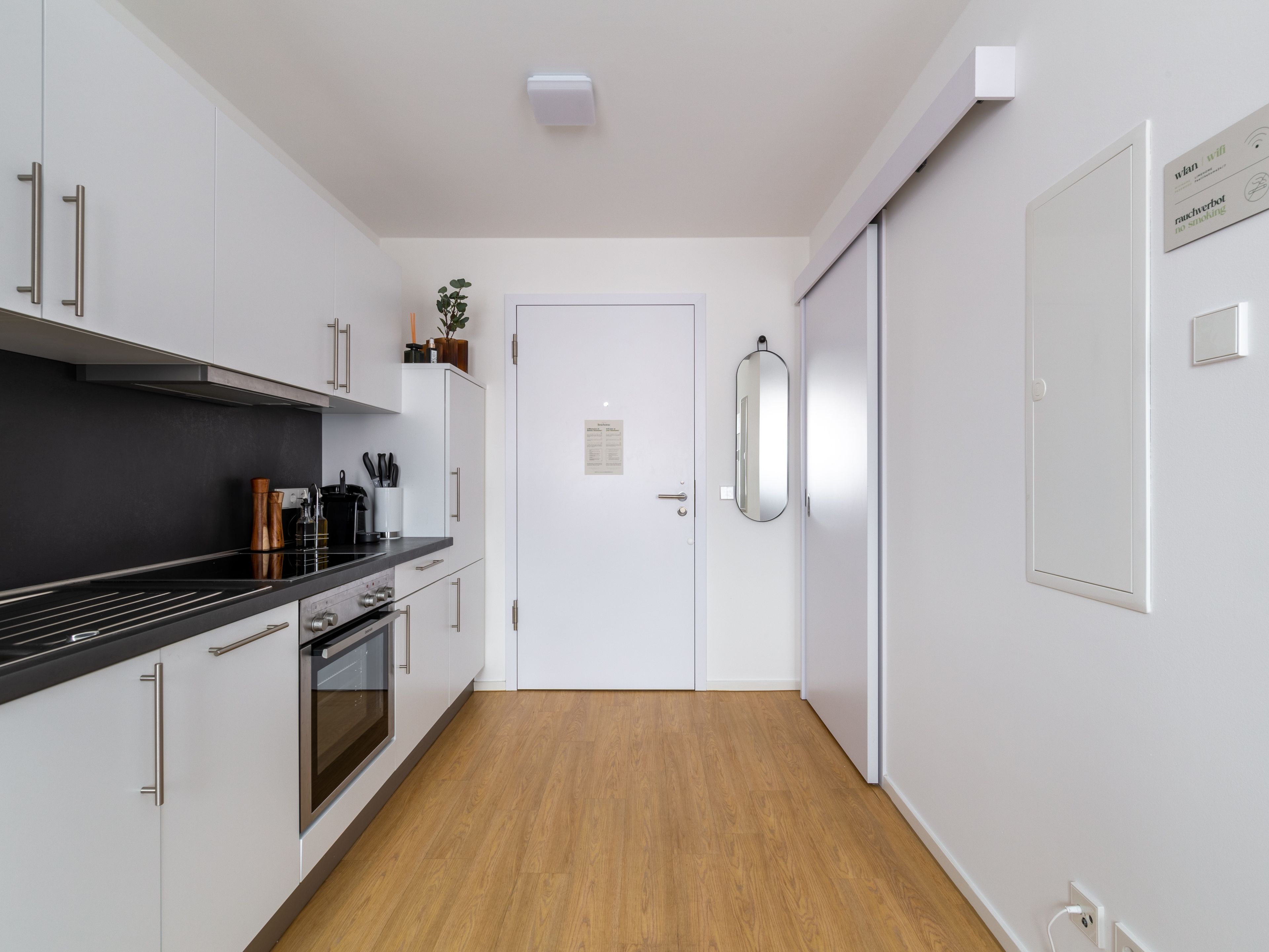 A modern kitchen with white cabinets, a black countertop, and a wooden floor.