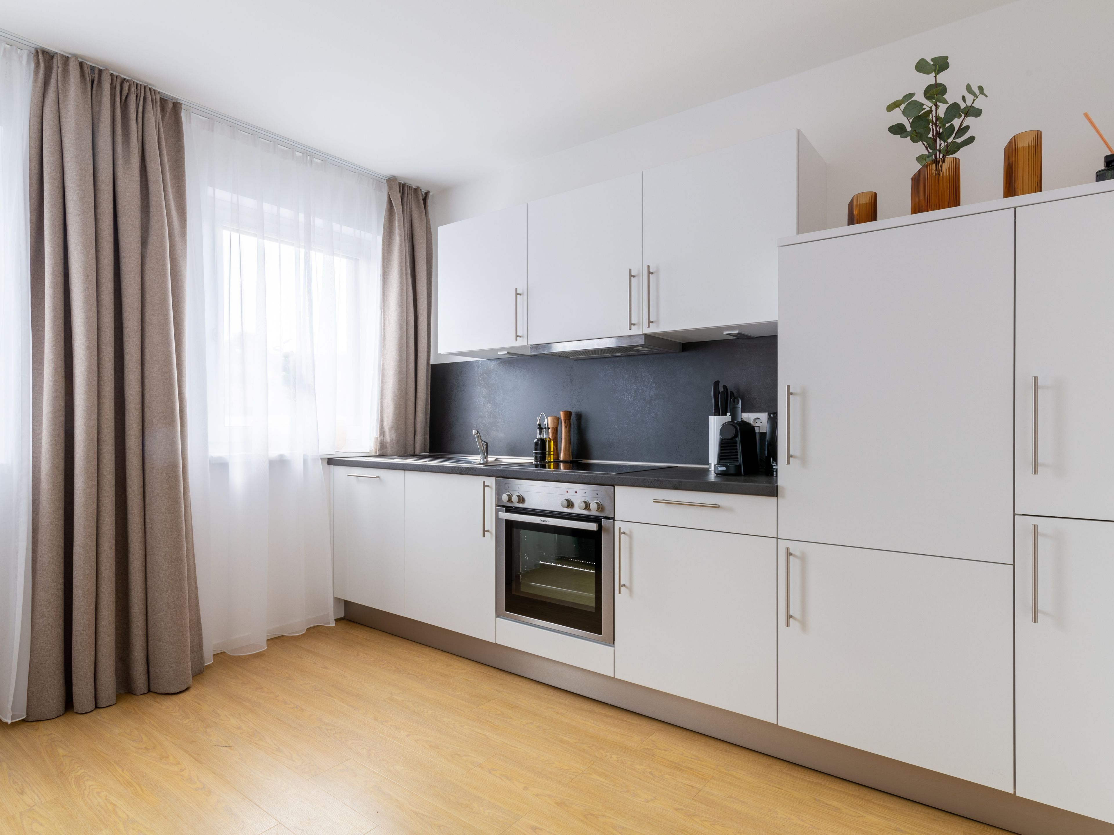 A modern kitchen with white cabinets, a built-in oven, and a black countertop.